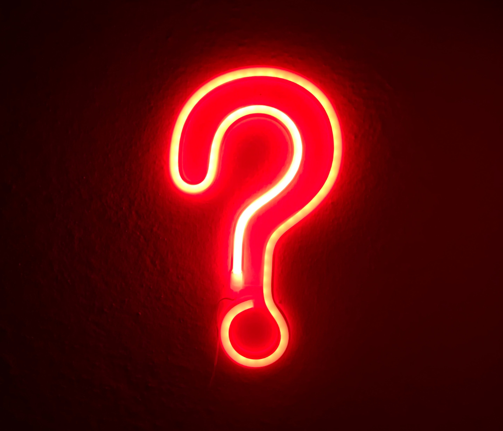 A neon red questions mark on a black background